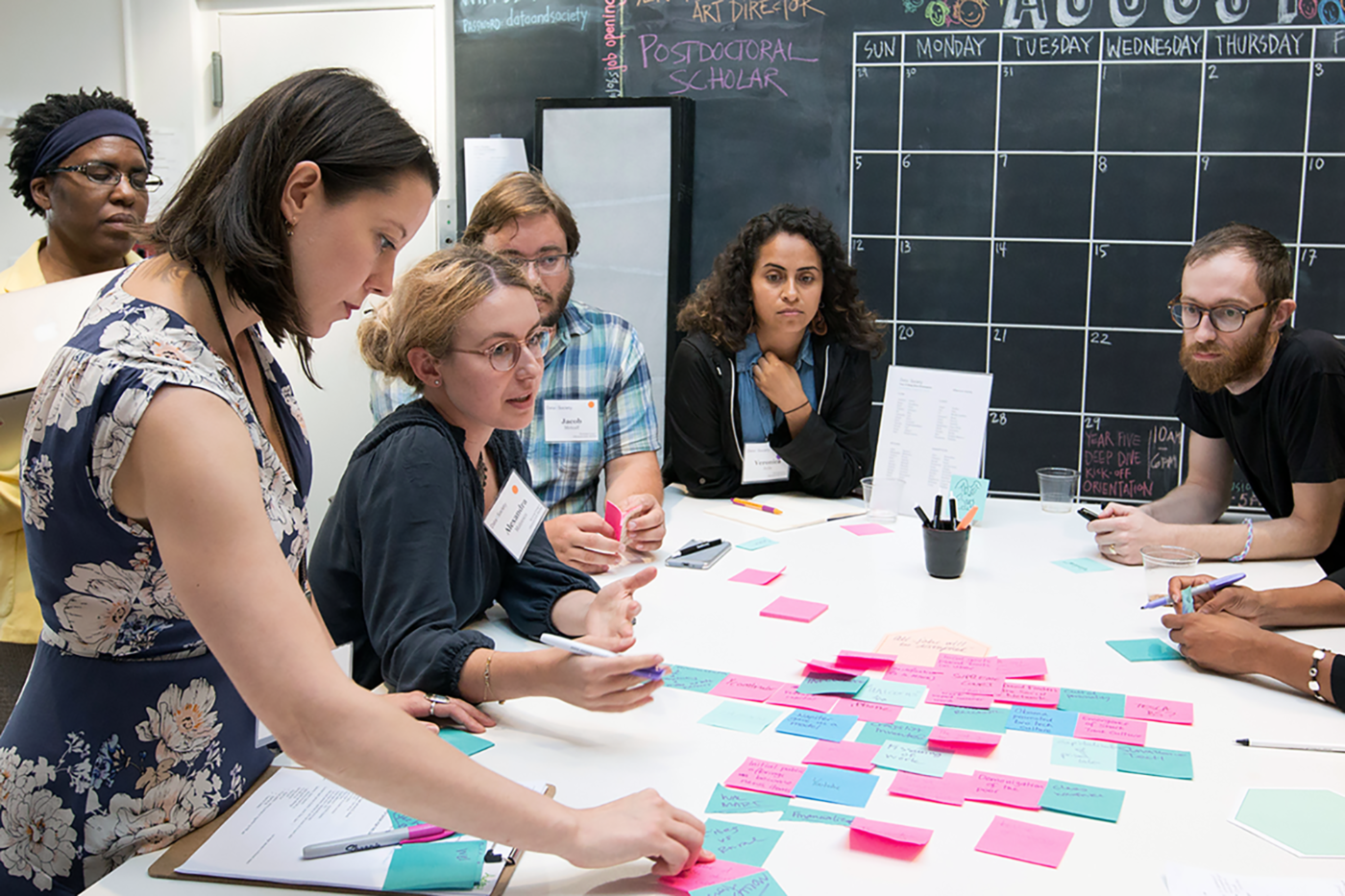 Group of people with serious expressions gathered around a white countertop with colorful post-it notes