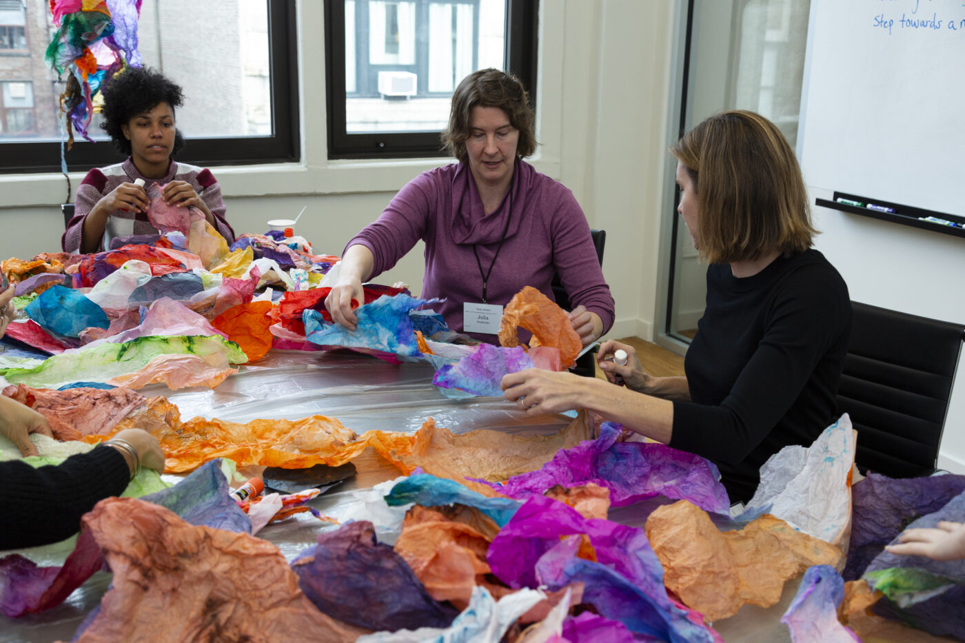 three women sitting at table covered with colorful tissue paper